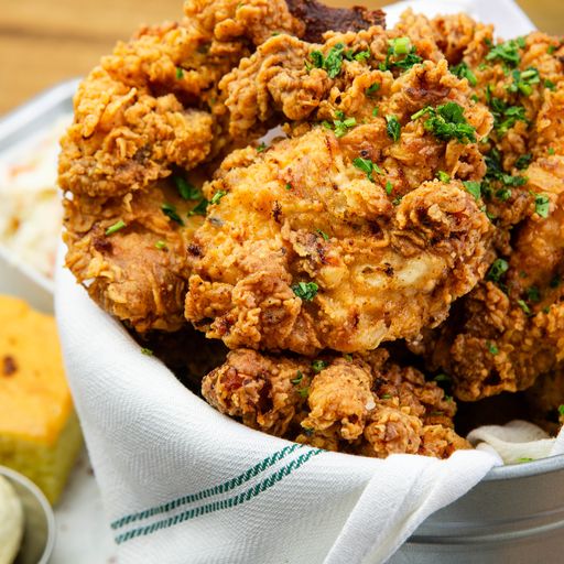Crispy fried chicken in a linen-lined bucket with cornbread and slaw